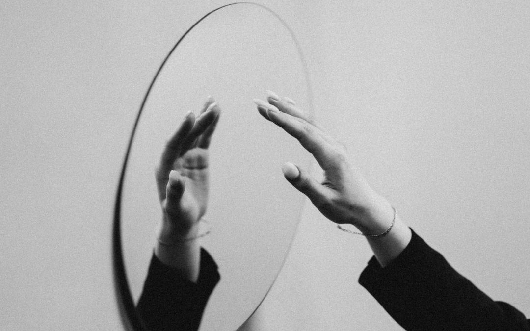 a hand reaching for, and reflected in, a round mirror on the wall
